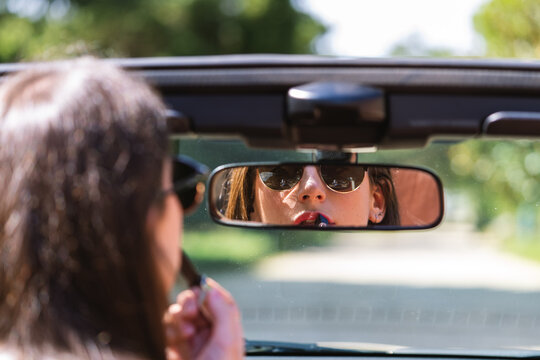 woman painting lipstick on the rearview mirror of her car 