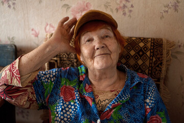 Portrait of elderly woman in blue floral blouse trying on cap indoors