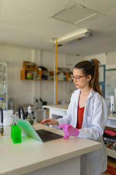 Positive young biologist using laptop in modern laboratory