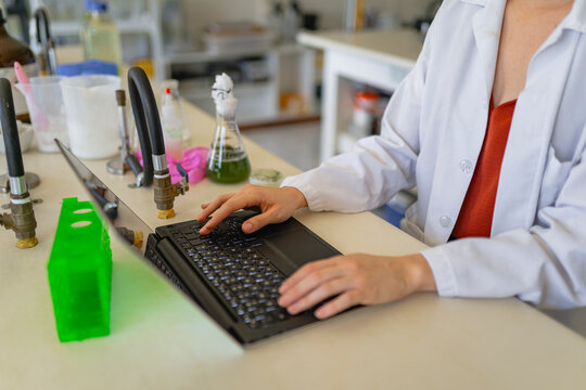 Crop female scientist using laptop while working in laboratory