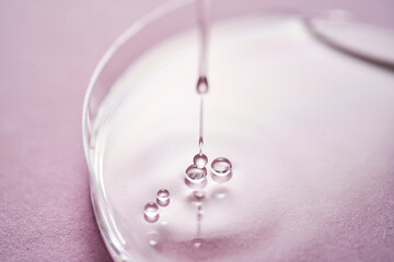 Serum or cosmetic oil flows into a transparent bowl on a purple background.