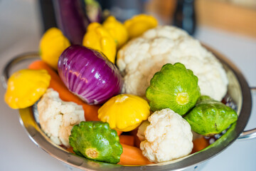 Fresh vegetables in a metal colander on a kitchen surface.