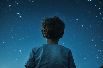 Rear view of a young boy looking up at a vast, starfilled night sky