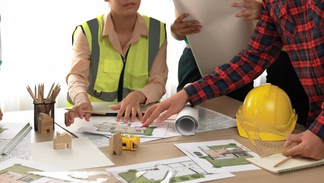 Smart architect and safety engineer discussion about building blueprint on table with architectural document, measurement tools and wooden block scatter around at modern office. Closeup. Delineation.