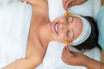 Smiling woman enjoying a facial massage with wooden rollers