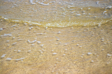 Gentle surf washing over the sandy shore at Surfside Beach, Texas. The close-up view highlights the sand's texture and the water's clarity, with small waves a summer travel destination. 
