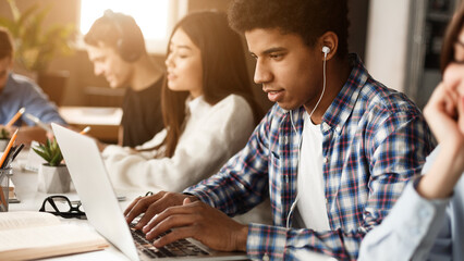 Student learning lessons in school library, making research on laptop and browse internet