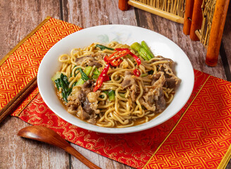 Lamb fried noodles with red pepper, chopsticks and spoon served in dish isolated on napkin side view on wooden table of taiwanese food