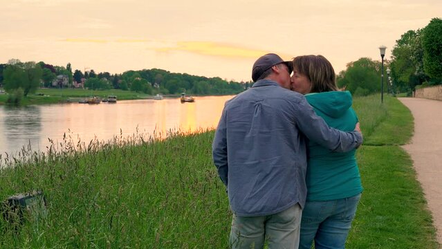 Close-up of a happy middle-aged married couple showing love and sincere feelings. They hug and kiss each other tenderly. enjoying  sunset together outdoors.