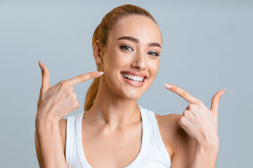 Orthodontic concept. Happy girl showing her beaming white teeth with two forefingers, grey background