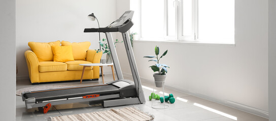 Interior of light living room with treadmill and yellow sofa