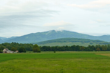 A Farmhouse in Front of Rolling Hills and Cloudy Mountains