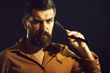 Portrait of brutal bearded man in stylish shirt with straight razor. Barbershop service. Hairdresser with barbershop accessories. Professional barber with vintage straight razor ready to shave beard.