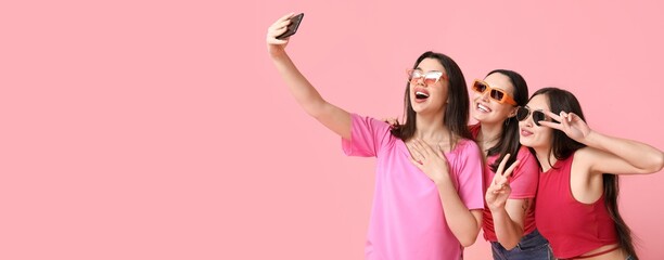 Beautiful young women in sunglasses taking selfie on pink background with space for text