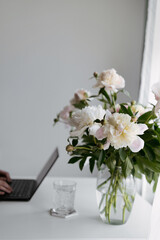 Aesthetic home office desk with laptop and white peony flowers in vase, grey background with copy space