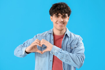 Handsome young man making heart with his hands on light blue background
