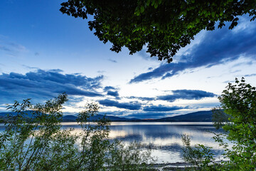 Krajobraz wodny, letni zachód słońca, piękny kolor, kolorowe niebo i chmury, jezioro w górach, kształt sylwetki, łodzie rybackie, widok na taflę wody, dzikie wybrzeże © anettastar