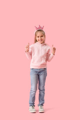 Cute little girl in crown and hoodie pointing at something on pink background