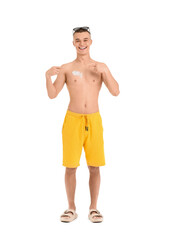 Fototapeta premium Happy young man in sunglasses pointing at sunscreen cream on his body against white background