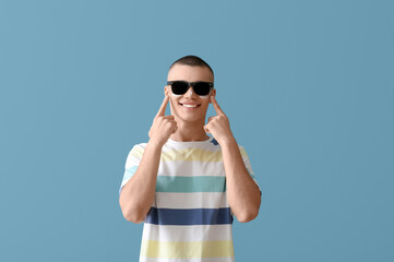 Happy young man in sunglasses with sunscreen cream on his face against blue background