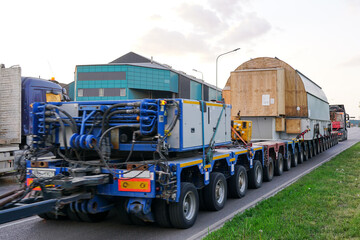 Very long specialized multi axle truck trailer carries very heavy oversize load, rear view