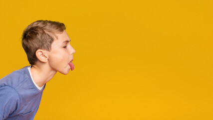 Little boy teasing someone, showing tongue and making face at free space aside, orange background