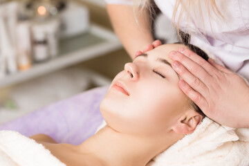 Young woman enjoying facial massage, lying on spa bed indoor at beauty salon.