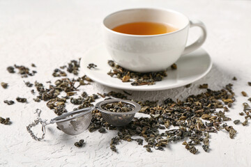 Cup of tea with infuser and dry green tea leaves on white textured background