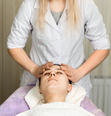 Young woman enjoying facial massage, lying on spa bed indoor at beauty salon.