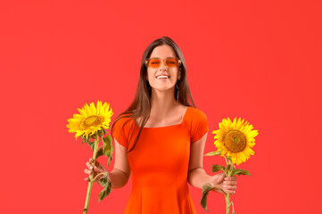 Young happy woman in sunglasses with beautiful sunflowers on red background