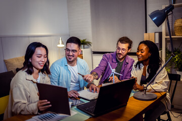 A group of four young people from diverse backgrounds gather around a model wind turbine. They share their thoughts and ideas about sustainable energy sources. 