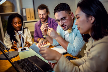 A group of four young people from diverse backgrounds gather around a model wind turbine. They share their thoughts and ideas about sustainable energy sources. 