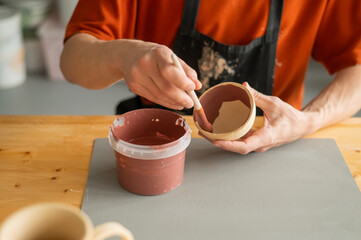 Close-up of a potter's hands with a brush painting ceramic dishes. 