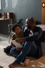 Vertical full length portrait of African American family of father and son using tablet together...