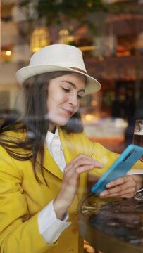 Trendy woman using mobile while having a beer in modern bar. Vertical space for text.