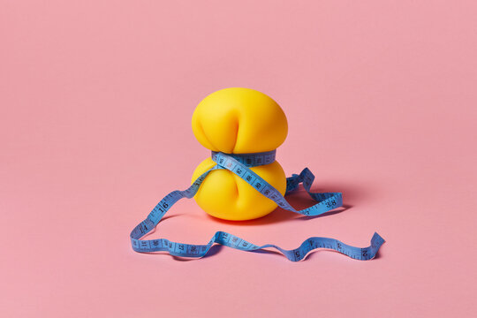 Yellow anti stress tied with blue measuring tape over pink background