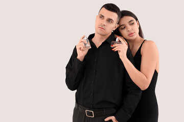 Elegant young couple with perfume on light background