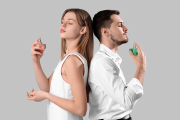 Young couple with bottles of perfume on light background