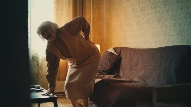 Senior woman feeling lower back pain while standing up from couch, arthritis