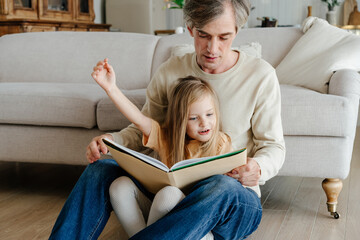 Father reading to daughter near couch
