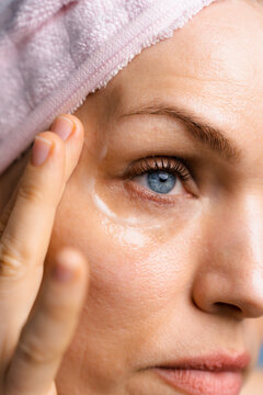 A woman applies cream to her lower eyelids