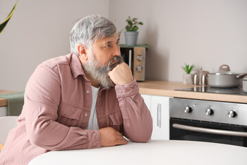 Portrait of sad senior man sitting at table in kitchen