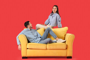 Obraz premium Beautiful young happy couple resting on sofa against red background