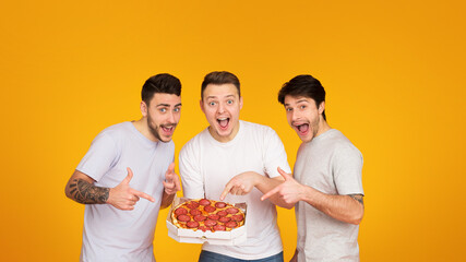 Three european men share a moment of joy as they open a box of pizza, a classic symbol of mateship,...