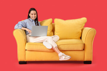 Beautiful young happy woman with laptop resting on sofa against red background