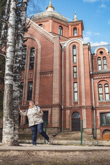 An elderly woman stands in front of a brick church.