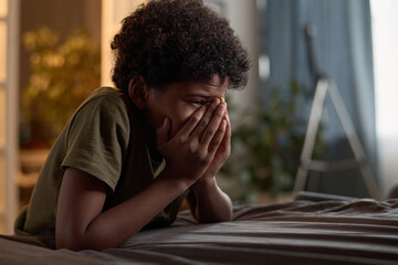 Side view portrait of hysterical young boy crying hiding in his room and covering face copy space