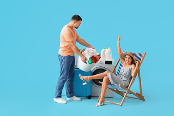 Young woman on vacation and her husband doing laundry on blue background