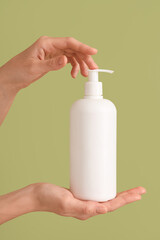 Female hands with bottle of cream against green background, closeup