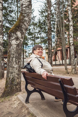 Fototapeta premium An elderly woman sits on a bench in a city park.